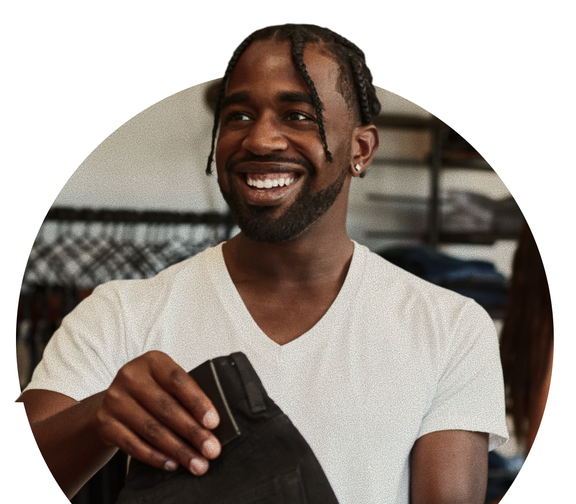 A person wearing a white t-shirt smiles while holding a pair of black pants in a clothing store.